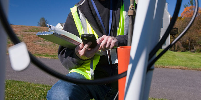Utility locator in green vest using phone to enter data.